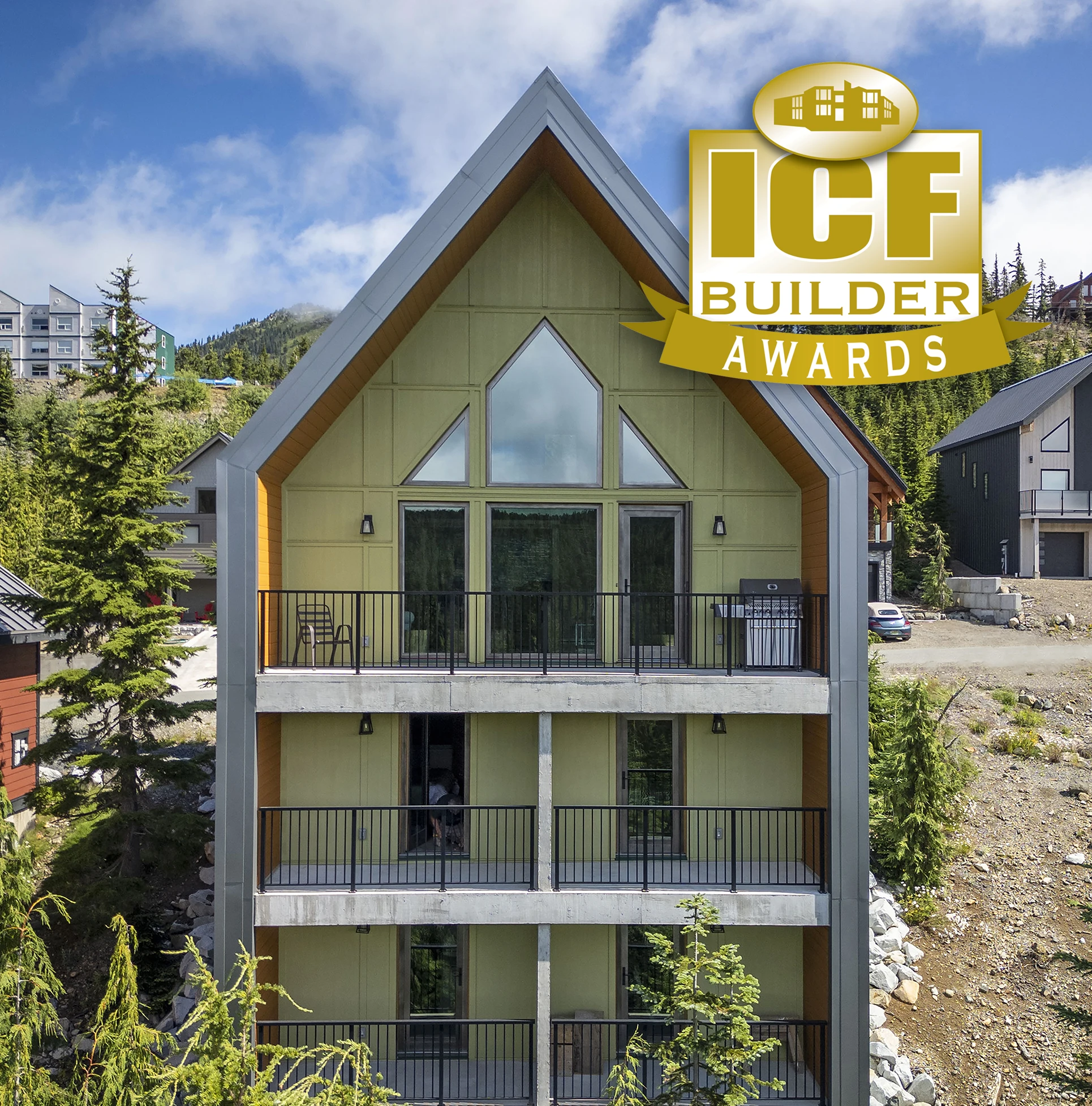 Green home with a steep pointed roof surrounded by trees.